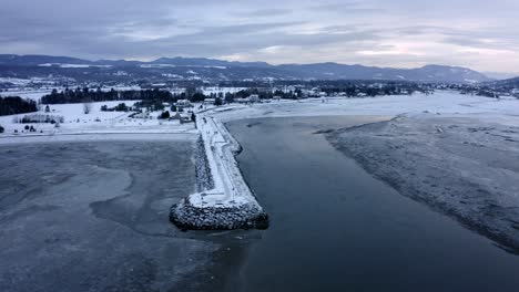 Toma-Aérea-Sobre-Un-Hermoso-Río-Y-Un-Pequeño-Pueblo-En-Un-Día-De-Invierno-En-Baie-Saint-paul