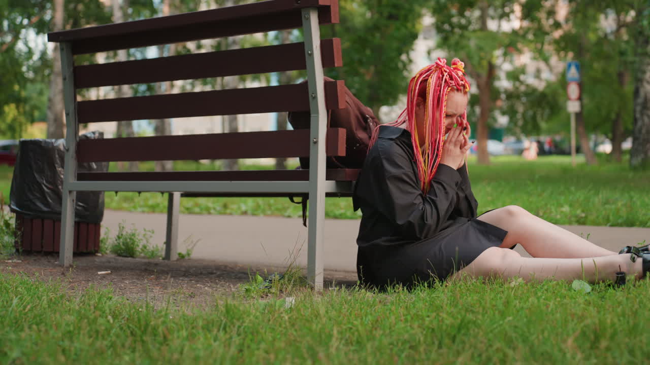 Una mujer con el pelo rosa se siente incómoda, una adolescente con rastas parece nerviosa al aire libre, una joven caucásica con el pelo rosa vibrante muestra preocupación en un parque urbano.