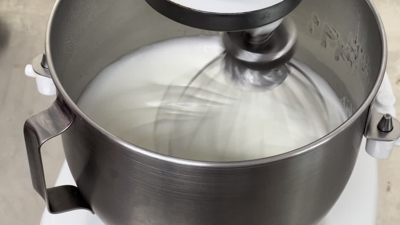 光沢のあるピークと硬いピークになるまで卵白と砂糖を混合し、メレンゲバタークリームを準備する電気ミキサーの接写、業務用キッチン設定