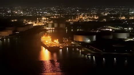 oil tanker docked at refinery reflects shimmering yellow light on water, aerial