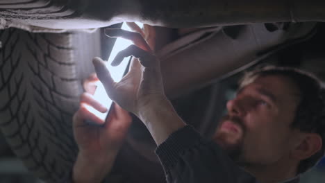 Primer-Plano-De-La-Mano-El-Mecánico-Inspecciona-El-Sistema-De-Escape-Del-Coche-En-El-Servicio-De-Coches.-Coche-En-El-Ascensor-Inspección-Y-Diagnóstico-De-Problemas-Con-La-Suspensión-Del-Coche