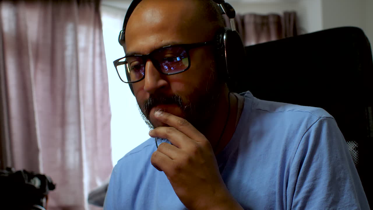 South Asian man wearing glasses and headphones listening to music at home