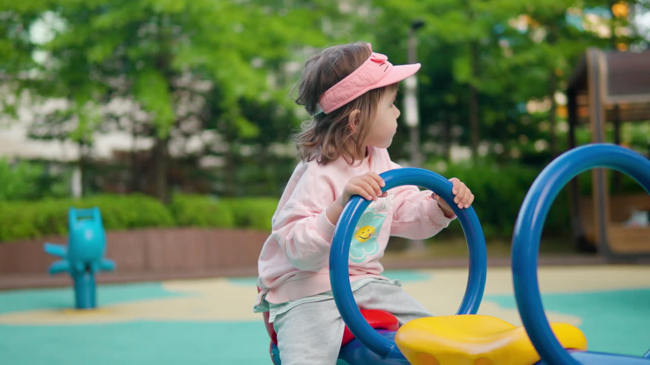 Niña pequeña se agarra del asa mientras se balancea en un subibaja de parque infantil.