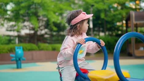 little girl holds handle while bouncing up and down on playground seesaw