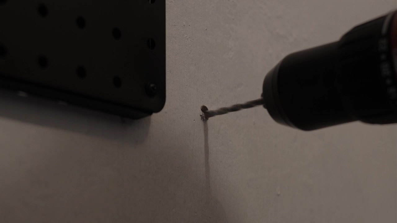 Close-up shot of a power drill creating a hole in an interior wall beside a black pegboard during installation