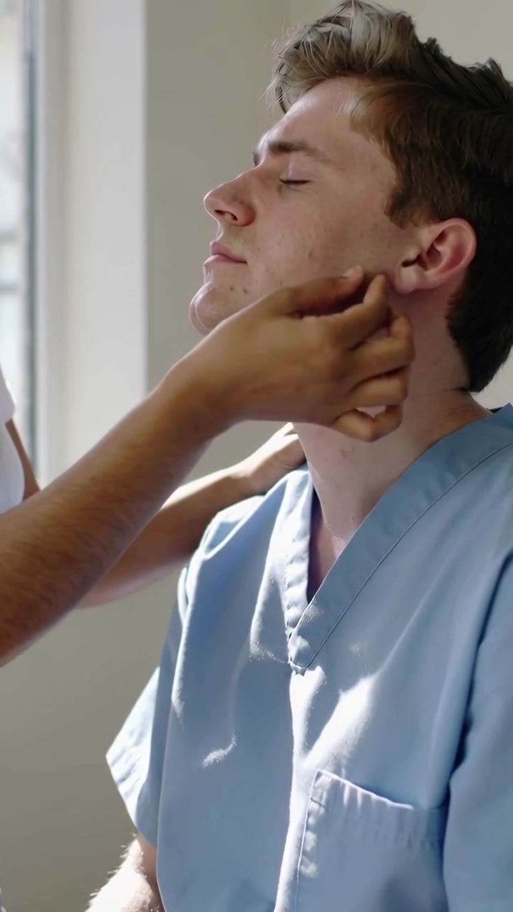 Video verticale: Uomo in divisa medica azzurra che inclina la testa mentre il medico gli palpa il collo in clinica per controllare la presenza di noduli.