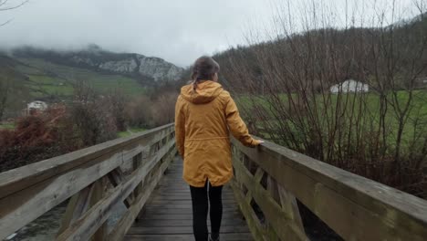 a young lady looks at the river below while walking across a timber bridge