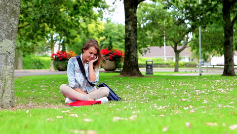 Estudiante-Feliz-Sentado-En-El-Césped-Haciendo-Una-Llamada-Telefónica