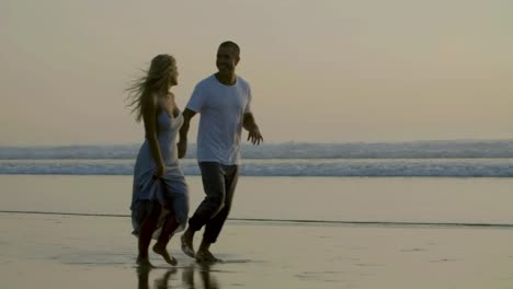 happy caucasian couple running along seashore at dawn.