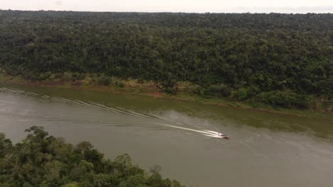 aerial birds eye shot of motorboat cruising over amazon river in amazon rainforest