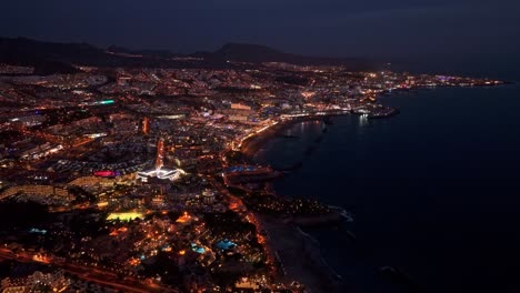 city lights of costa adeje on island of tenerife, canary islands, aerial at night, slow tracking right to left, wide angle establishing view.