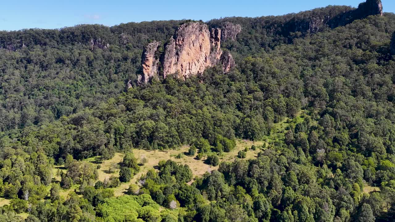 Aerial footage captures the iconic Nimbin Rocks surrounded by dense forest under bright daylight, showcasing natural beauty and geological formations