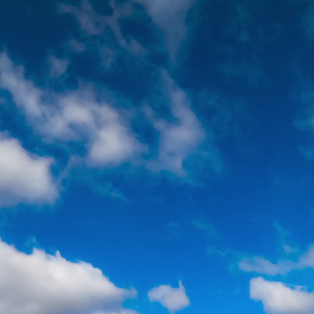 Blue summer sky with little soft white clouds floating quickly. Low angle view. Timelapse