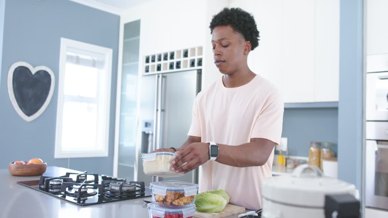 Un uomo afroamericano sistema contenitori impilati sull'isola della cucina, disimpilandoli per la preparazione dei pasti.