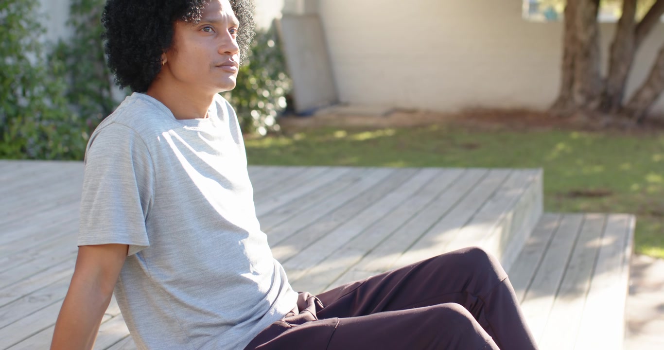 Kameraet trækker sig tilbage, og en afroamerikansk mand sidder på trætrin i sorte sneakers og reflekterer.