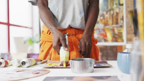 Midsection-of-african-american-male-painter-mixing-paint-in-artist-studio