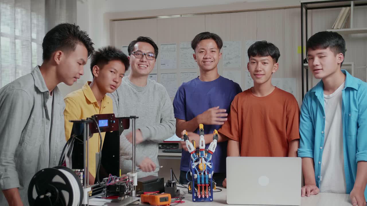 과 3d 프린팅을 가진 아시안 남자와 소년들은 학교에서 사이보그 손에 대해 논의하는 동안 미소 짓고 카메라에 팔을 고 있습니다.