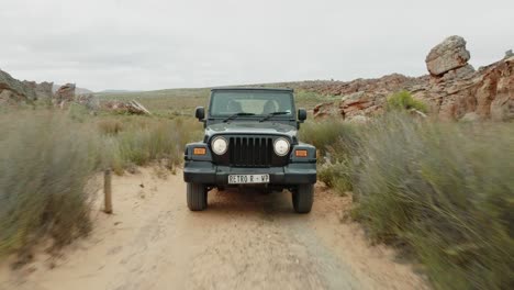 drone flies fast backwards over ground in front of a black off-road vehicle over desert landscape and through rock formations in cederberg wilderness area in south africa