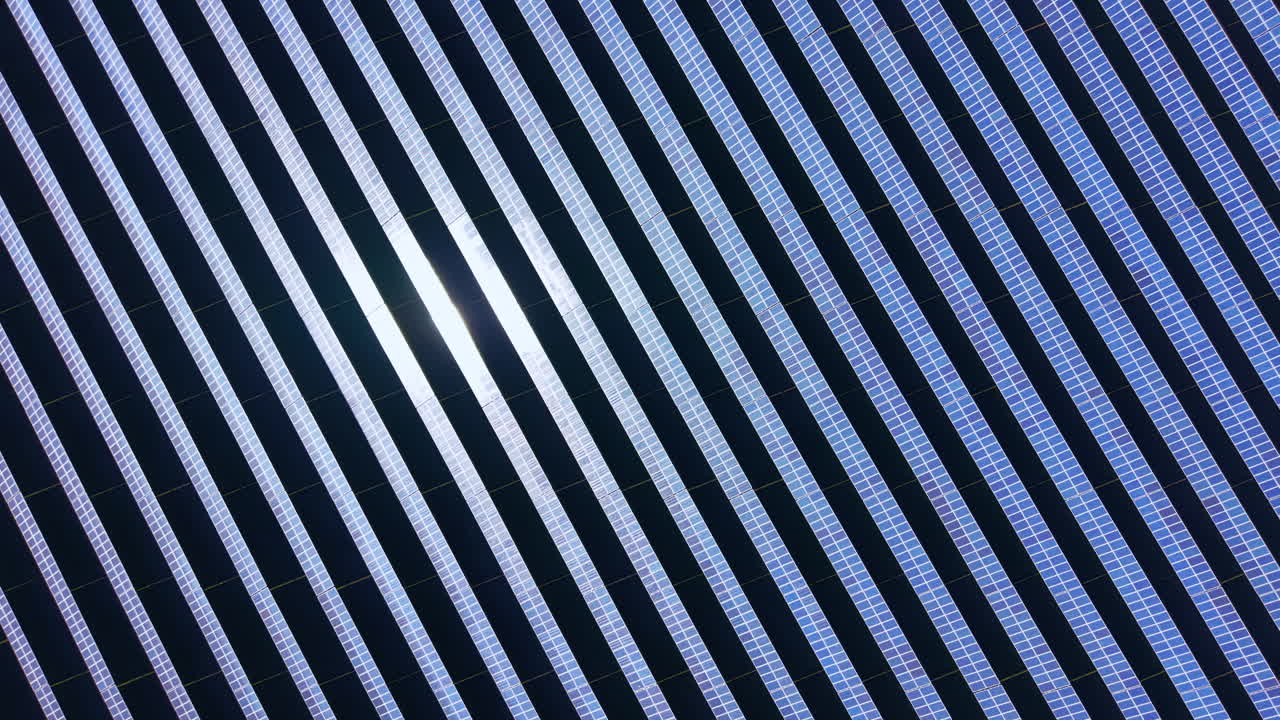 Solar panels arranged in neat rows capture sunlight in a large solar farm in the countryside during midday