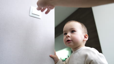 happy toddler boy switches on the light in the room. mom's hand switches off the light. baby playing with illumination. low angle view.