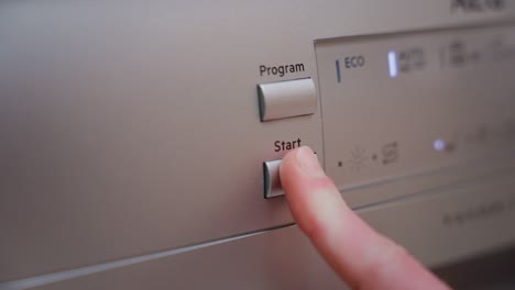 man hand press start button on dishwasher