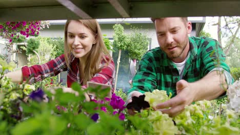 smiling young man and woman gardeners taking care of flowers and plants