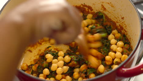 dumping chickpeas into a red paste or sauce simmering in the pot on the stove then mixing