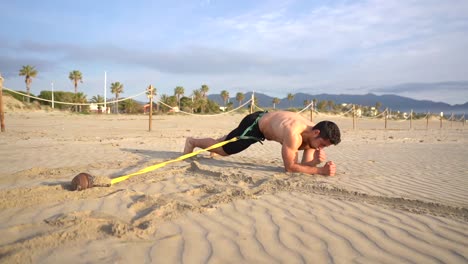 shirtless muscular guy doing planks on elbows crawling through sand