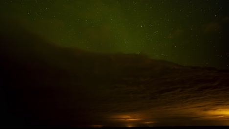 beautiful time lapse of green northern lights above dark clouds with a starry night sky with shooting stars