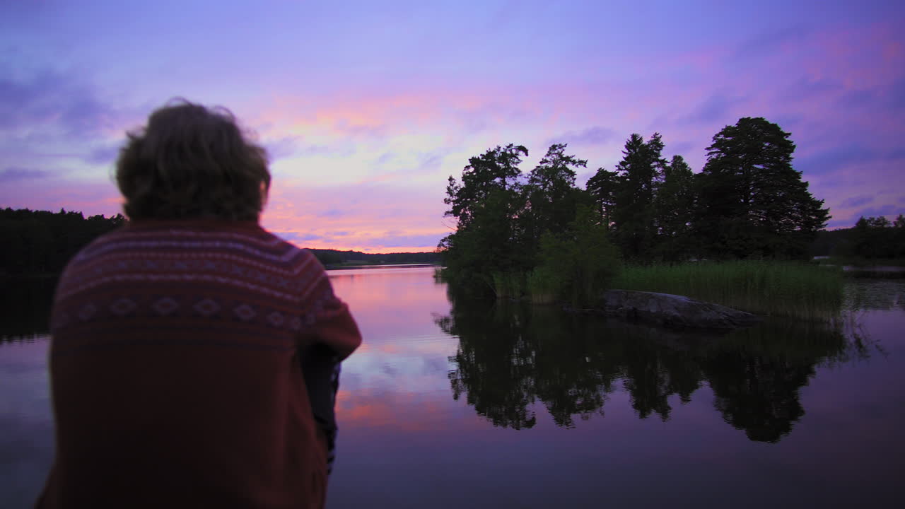 caminando hacia un hombre sentado en una orilla rocosa, de un lago, un cielo púrpura, en una colorida puesta de sol o anochecer, en el fondo, en albysjon, tyreso, suecia
