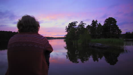 Auf-Einen-Mann-Zugehen,-Der-An-Einem-Felsigen-Ufer-Sitzt,-An-Einem-See,-An-Einem-Violetten-Himmel,-Bei-Einem-Farbenfrohen-Sonnenuntergang-Oder-In-Der-Abenddämmerung,-Im-Hintergrund,-In-Albysjon,-Tyresö,-Schweden
