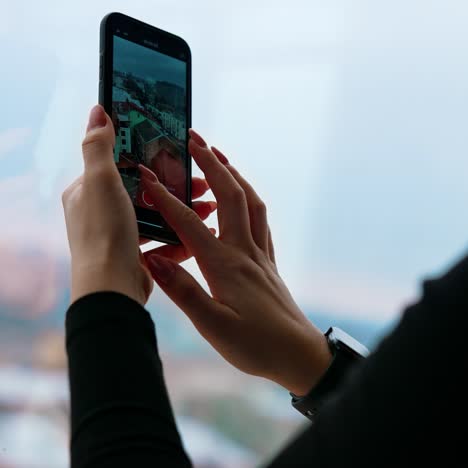 girl with a mobile phone indoors. young woman taking photo of a cityscape through the office window. close-up