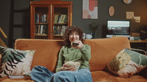 laughing woman eating popcorn and watching funny tv show at home