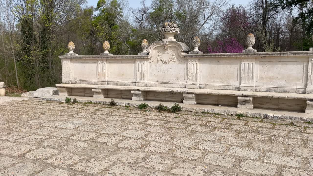 съемки внушительных неоклассических известняковых скамей с прочной и элегантной структурой, расположенных на мощенной тропе в зеленой зоне королевского дворца аранхуэса