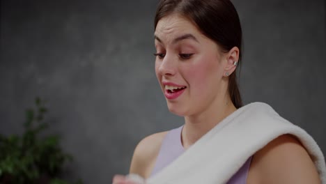 primer plano una chica morena segura y cansada en una camiseta deportiva púrpura se limpia los restos de sudor con una toalla blanca después de un intenso ejercicio en un apartamento moderno en casa