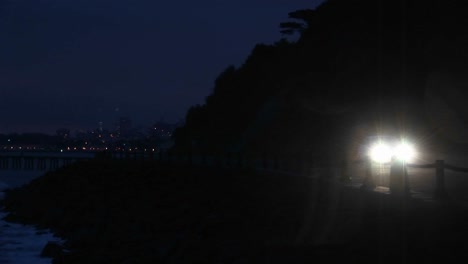 a car's headlights brighten a dark road on the far side of a bay