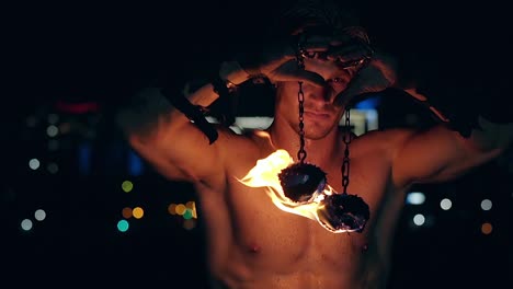 Young-blond-male-holds-two-pois-hanging-on-chains-raises-them-then-lowers-them-Male-stares-at-camera