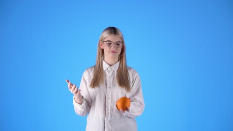안경을 쓴 젊은 금발 백인 여성은 오렌지 과일 스튜디오에서 무한한 크로마 배경 몸통 으로 놀고 있습니다.