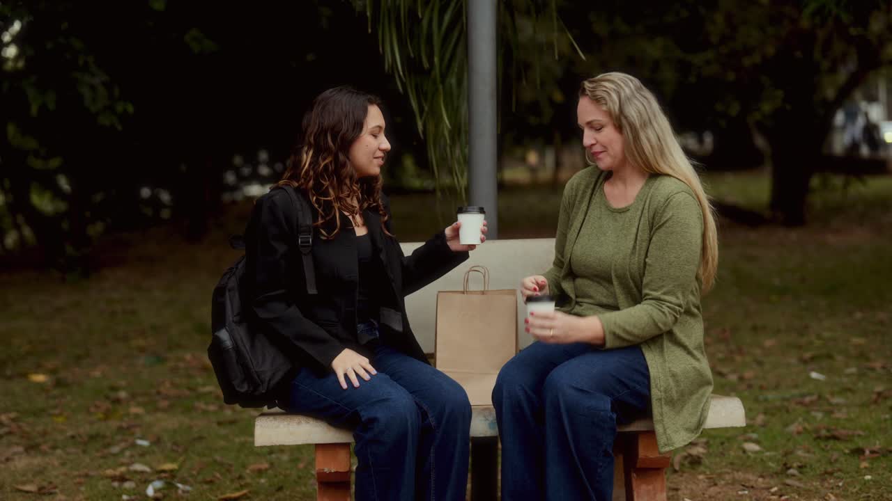 Two women friends enjoy coffee and conversation on a park bench