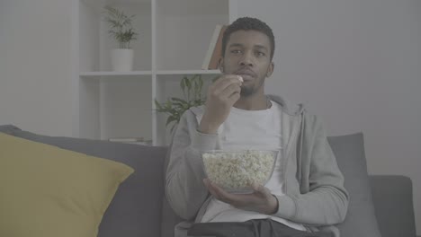 young african american male watching attentively a movie and eating popcorn