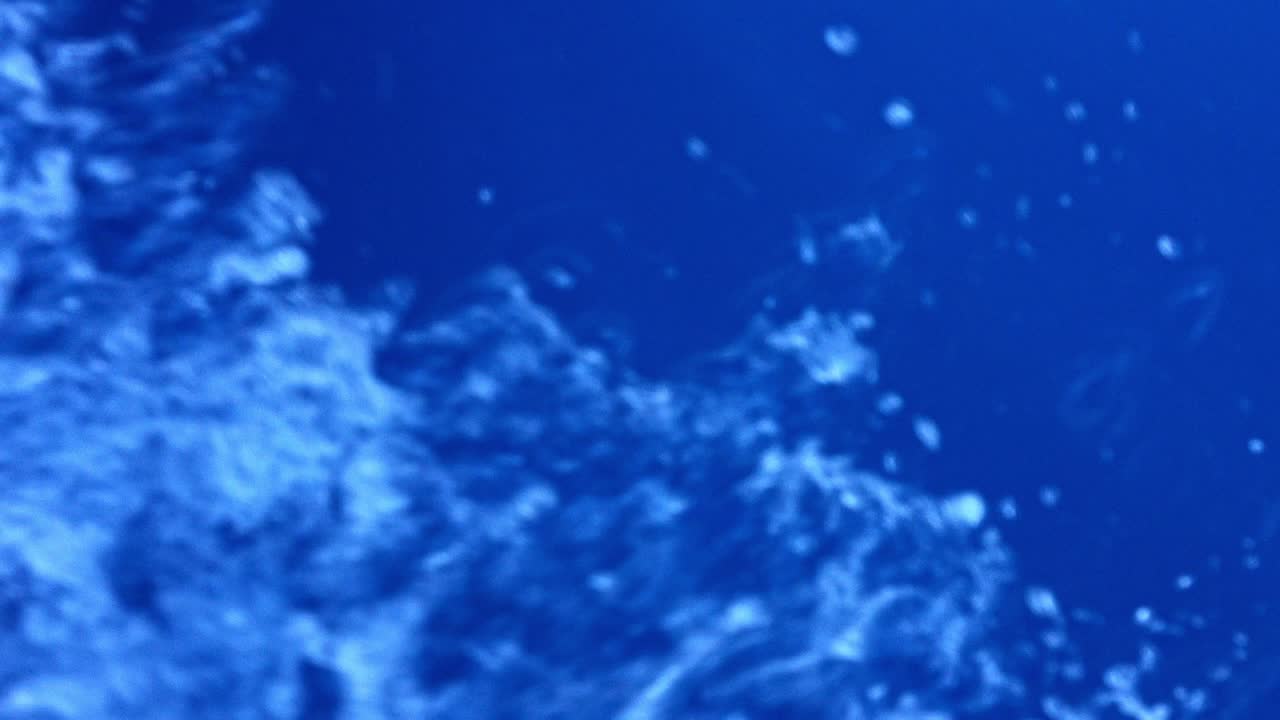 Scatto astratto di acqua che schizza nell'oceano aperto con i raggi del sole che trafiggono l'azzurro.