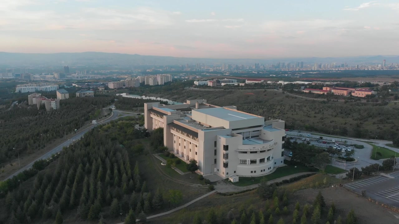 Tomada rotativa em torno de uma sala de concertos em campus universitário com horizonte da cidade ao fundo (Aéreo 4K)