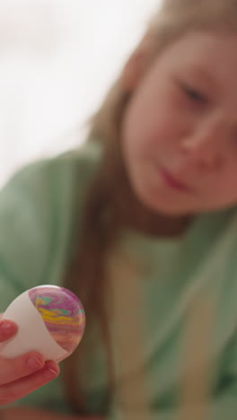 curious little girl looks at easter egg with abstract marbling patterns in studio closeup slow motion. preparing for spring holiday with children