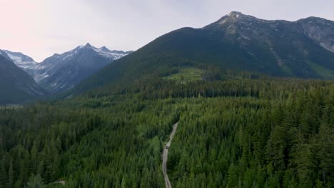 road through greenery forest in highway 99 with towering mountainscape background in british columbia, canada