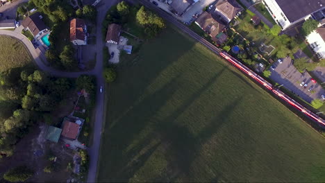 Aerial-view-of-a-red-train-and-a-car-entering-a-village