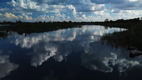 wide shot with a slow jib down revealing a pond surface with majestic clouds reflecting in the water