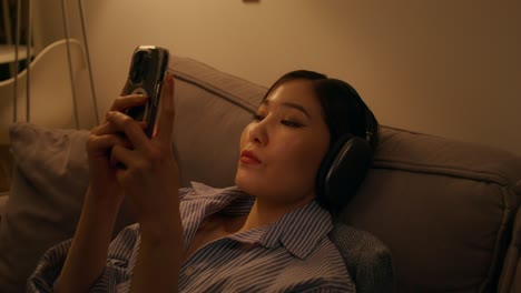 헤드폰과 전화로 집에서 휴식을 취하는 여자
