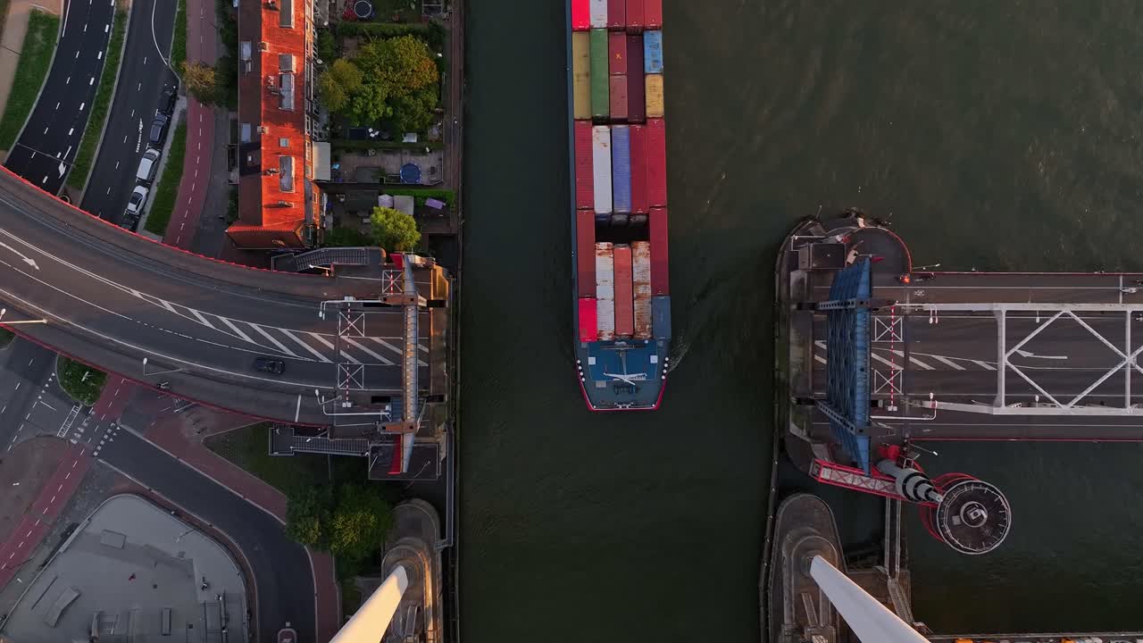 Top down view of a container barge sailing between an open bridge on a sunny evening