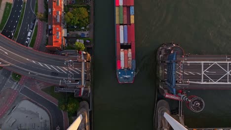 Top-down-view-of-a-container-barge-sailing-between-an-open-bridge-on-a-sunny-evening