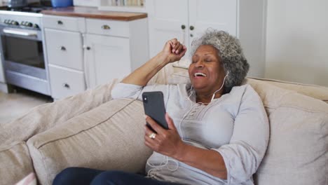 Ältere-Afroamerikanische-Frau-Mit-Kopfhörern,-Die-Zu-Hause-Einen-Videoanruf-Auf-Dem-Smartphone-Führt